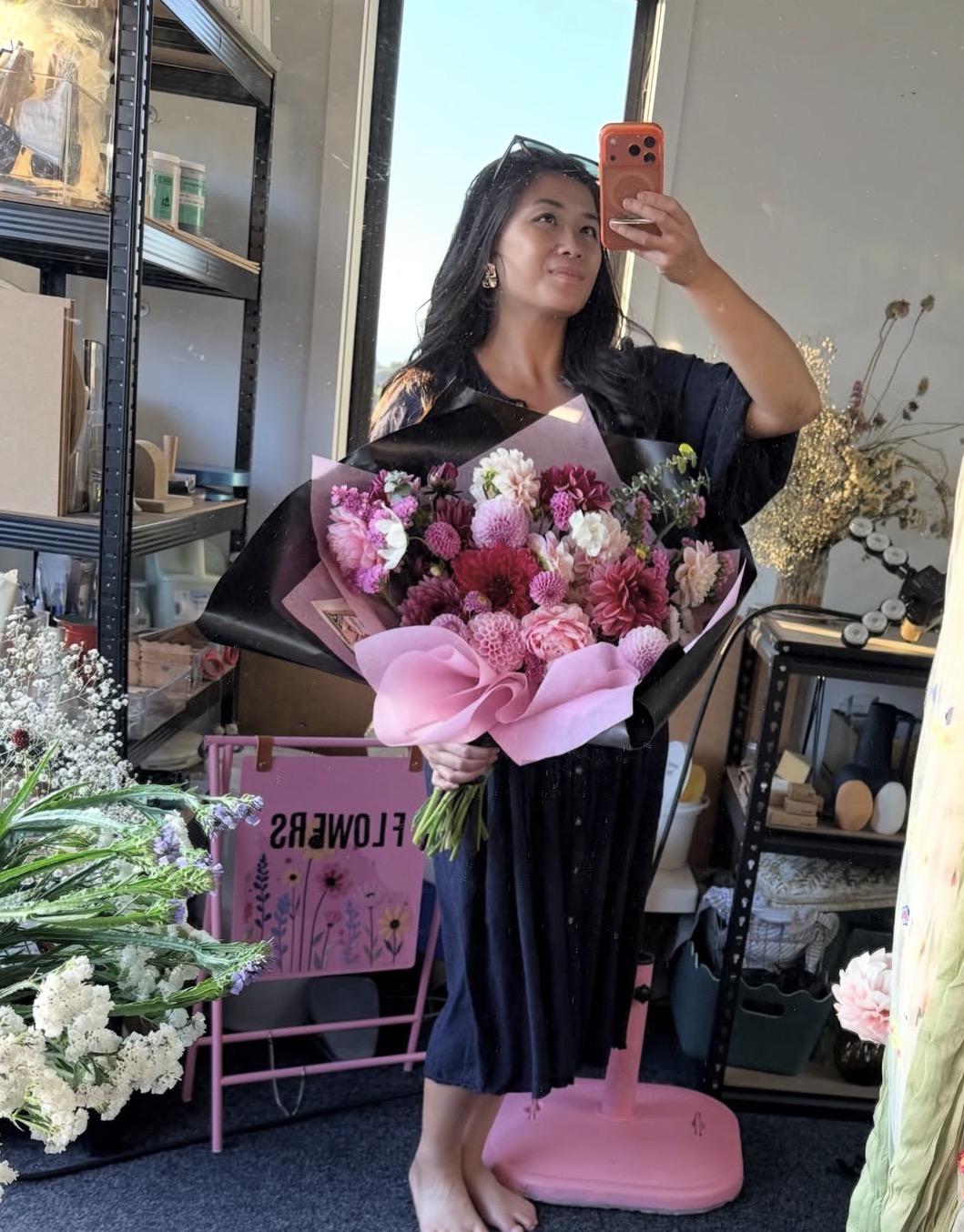 Mia holding a large bouquet of pink and burgundy dahlias in her florist studio.